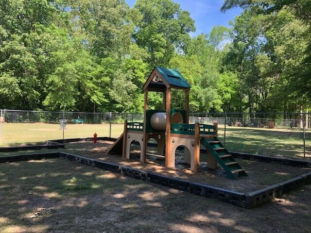 Memphis Dog Parks, Dog-Friendly Breweries & More - 2 A small playground structure with a slide, tunnel, and steps is set in a fenced outdoor area surrounded by trees on a sunny day, similar to those found at memphis dog parks.