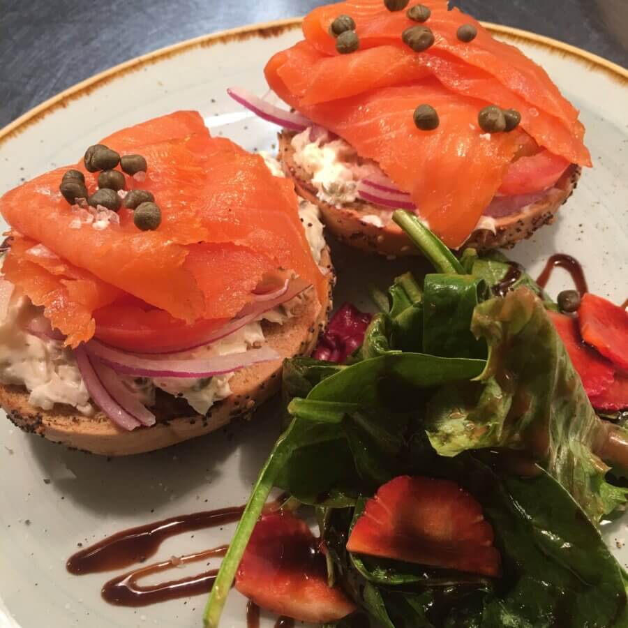 The Best Brunches in Louisville: 13 Must-Try Spots - 10 Two bagel halves topped with cream cheese, smoked salmon, red onion, tomato, and capers, served with a side salad of greens and sliced strawberries drizzled with balsamic glaze—perfect for the best brunch in Louisville.
