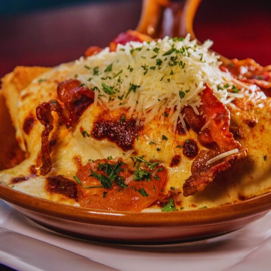 The Best Brunches in Louisville: 13 Must-Try Spots - 9 A baked dish topped with melted cheese, crisp bacon, sliced tomatoes, shredded parmesan, and chopped herbs, served in a brown ceramic bowl—an ideal choice for the best brunch in Louisville.