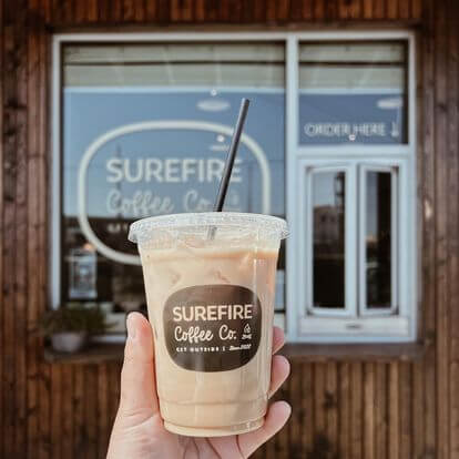 A hand holding iced coffee in from of Surefire window.