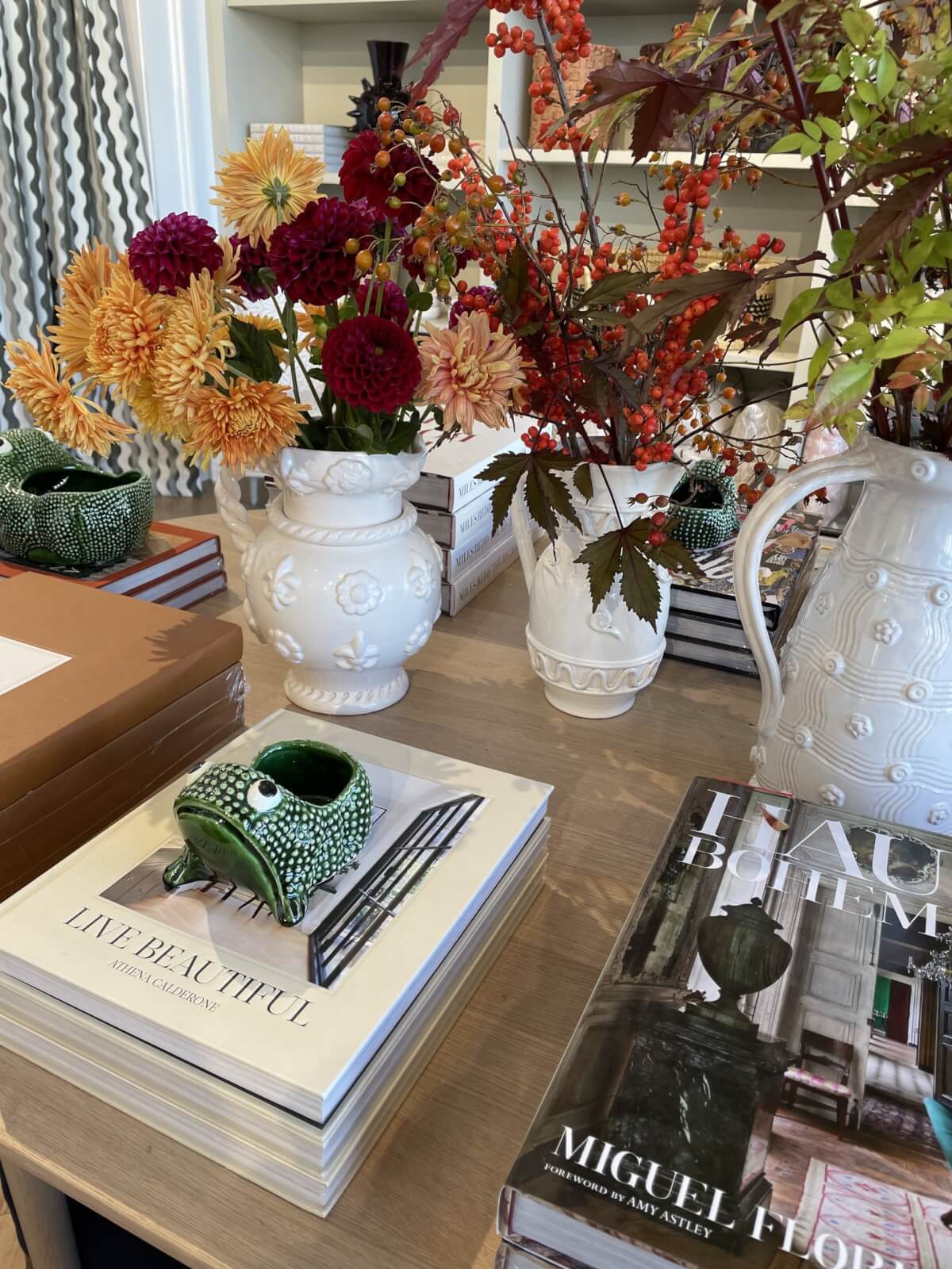 White vases with autumn florals by coffee books.