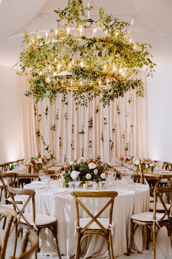 A close-up of a reception table with a greenery-laden chandelier overhead.