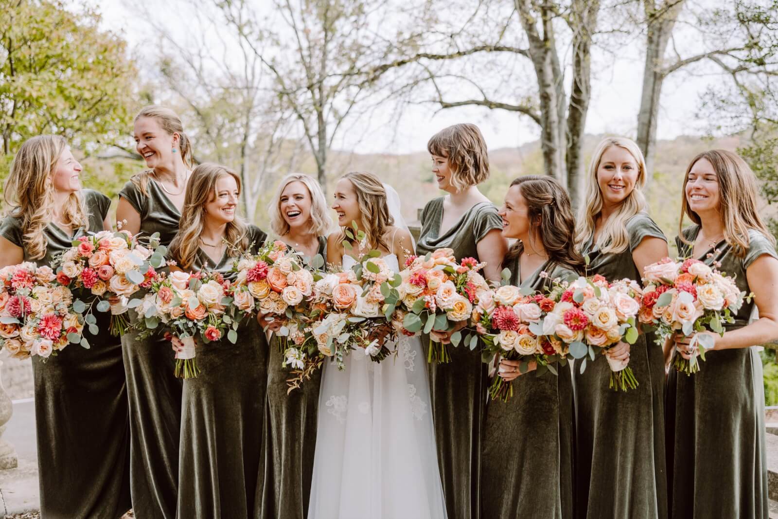 The bride smiles and laughs with her bridesmaids, who wear sage green.