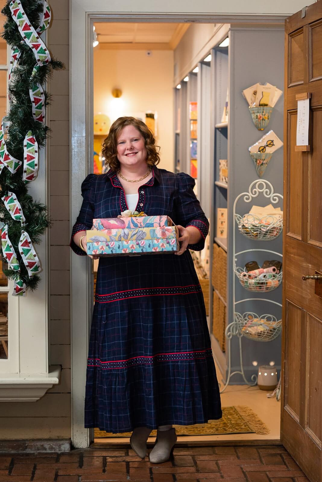Vanessa West holding three wrapped gifts in a doorway.