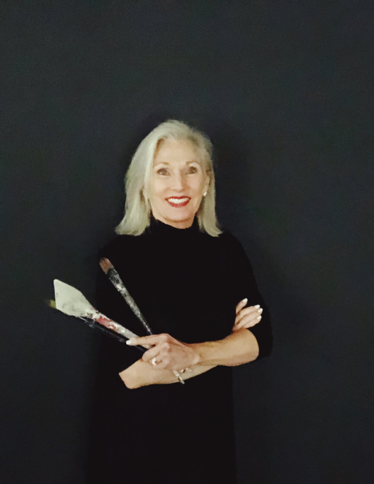 Martha Nemer holding paint brushes against a black background.