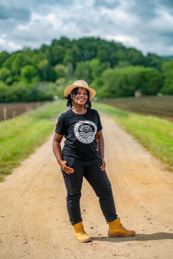 Farmer Cee Stanley in a black Green Heffa Farms t-shirt smiling on a dirt road on her farm