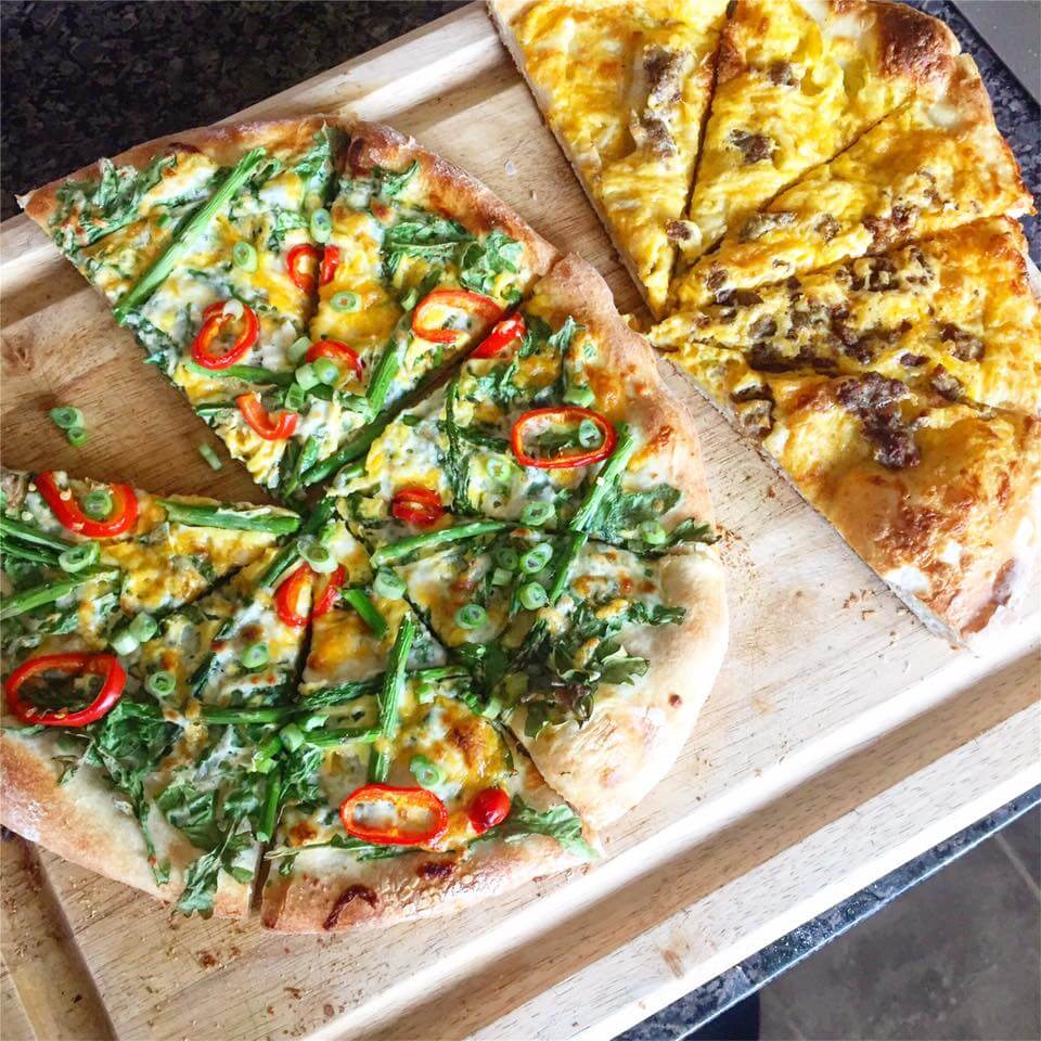 Two sliced pizzas on a wooden cutting baord.