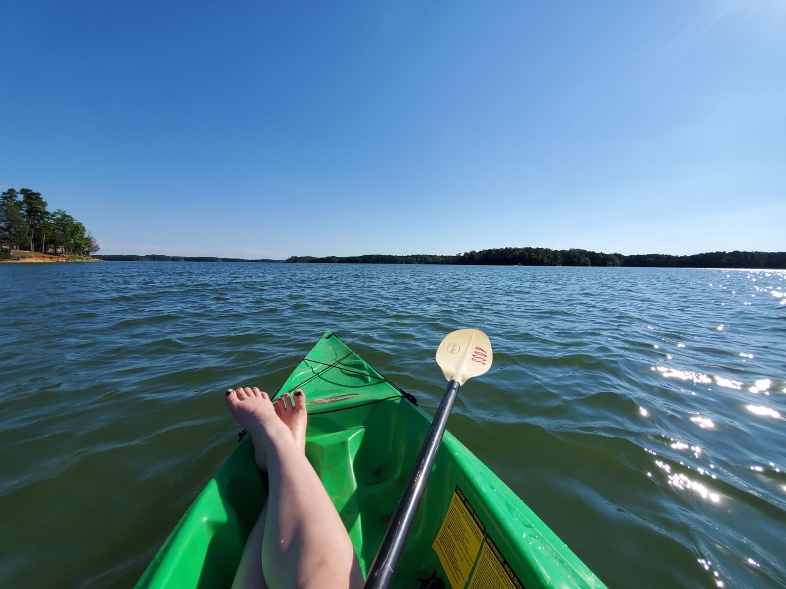 Woman with legs crossed in green kayak on the water.