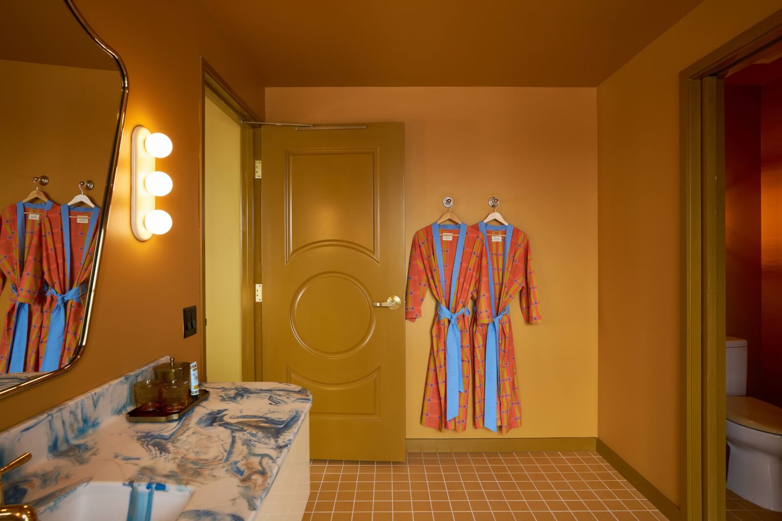 Yellow bathroom with two robes hanging on the wall.