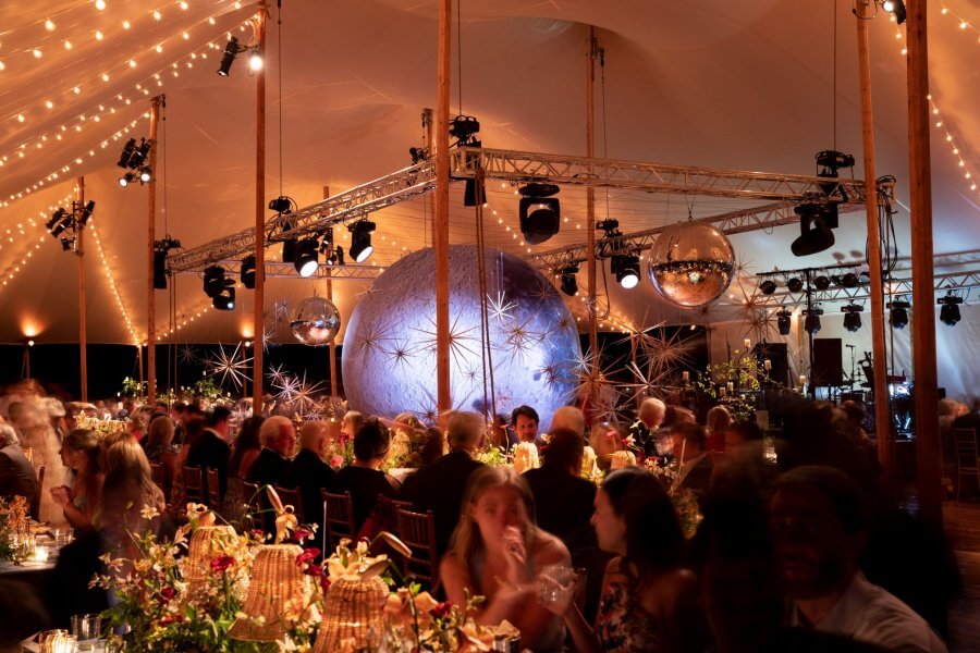A Wild Storybook Wedding You Won't Believe - 22 Guests enjoying seated dinner under a wedding tent with lit up moon in the middle of the dance floor