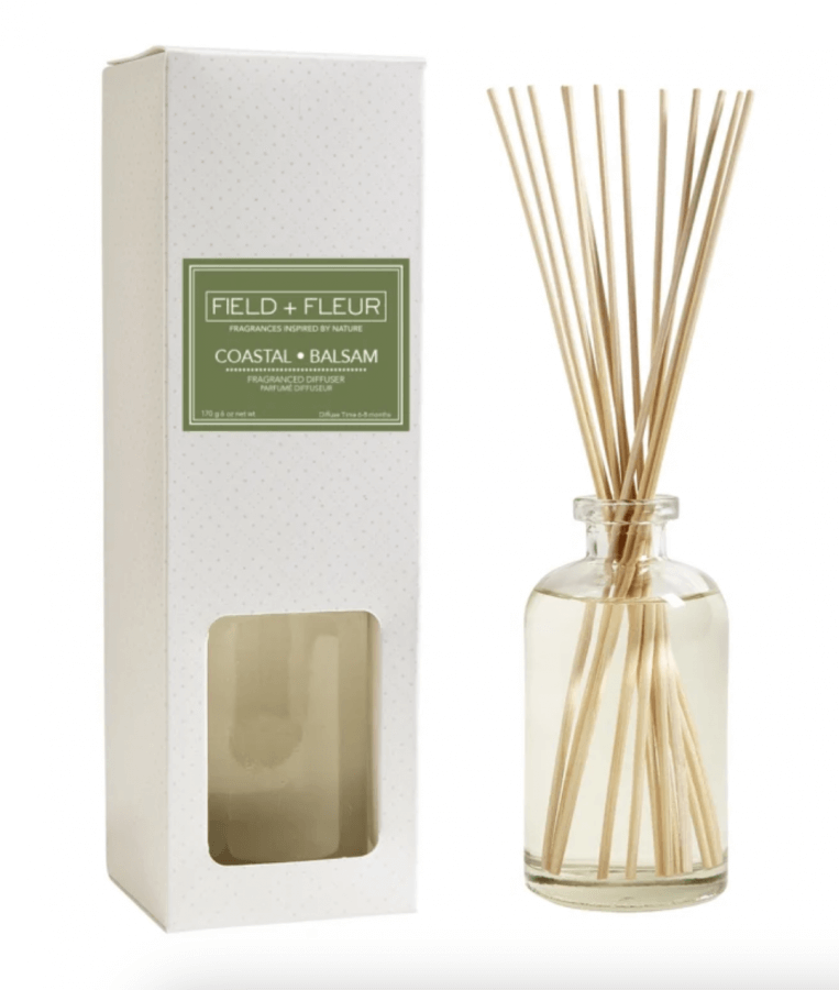 A box and a glass bottle of reed diffusers labeled "Coastal Balsam" by Field + Fleur, a perfect summer find. The bottle contains fragrance oil and multiple reed sticks.