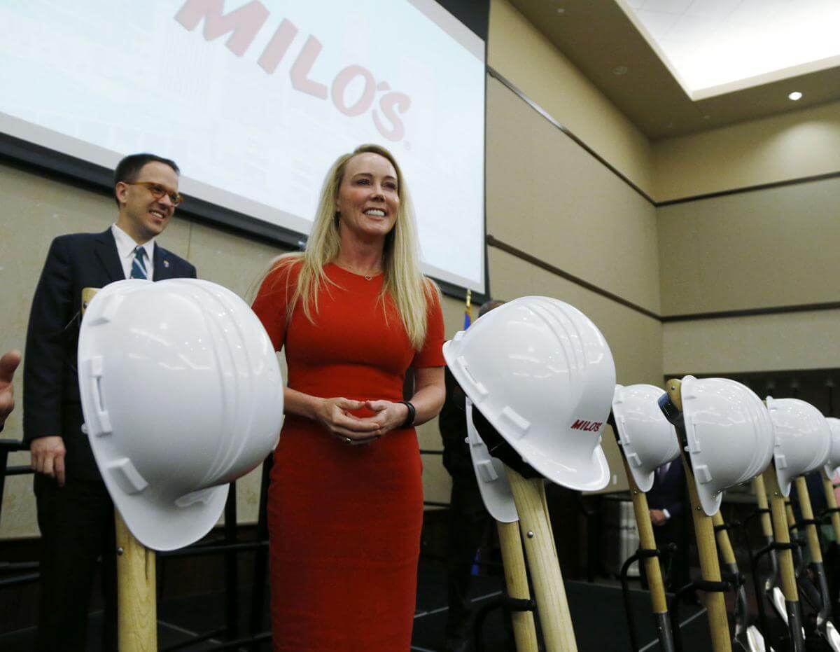 Blonde woman in red dress posing next to white hard hats. 