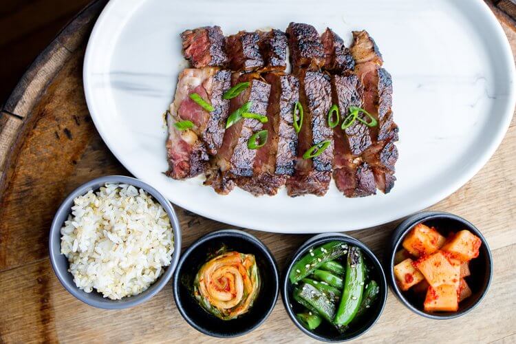 Korean meat on a white plate surrounded by various toppings and sides.