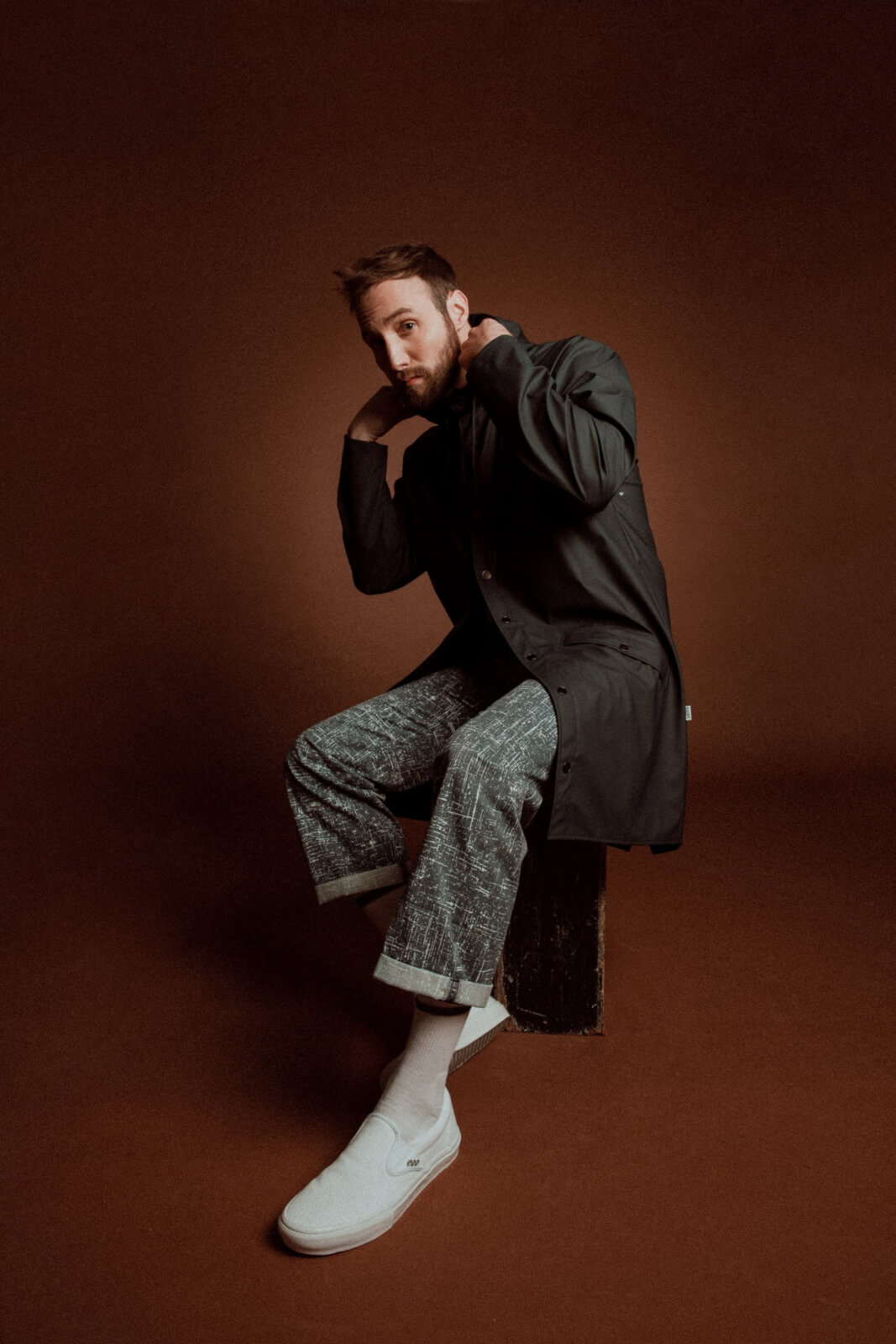 Ruston Kelly sitting on a chair in front of a brown background, adjusting coat collar.