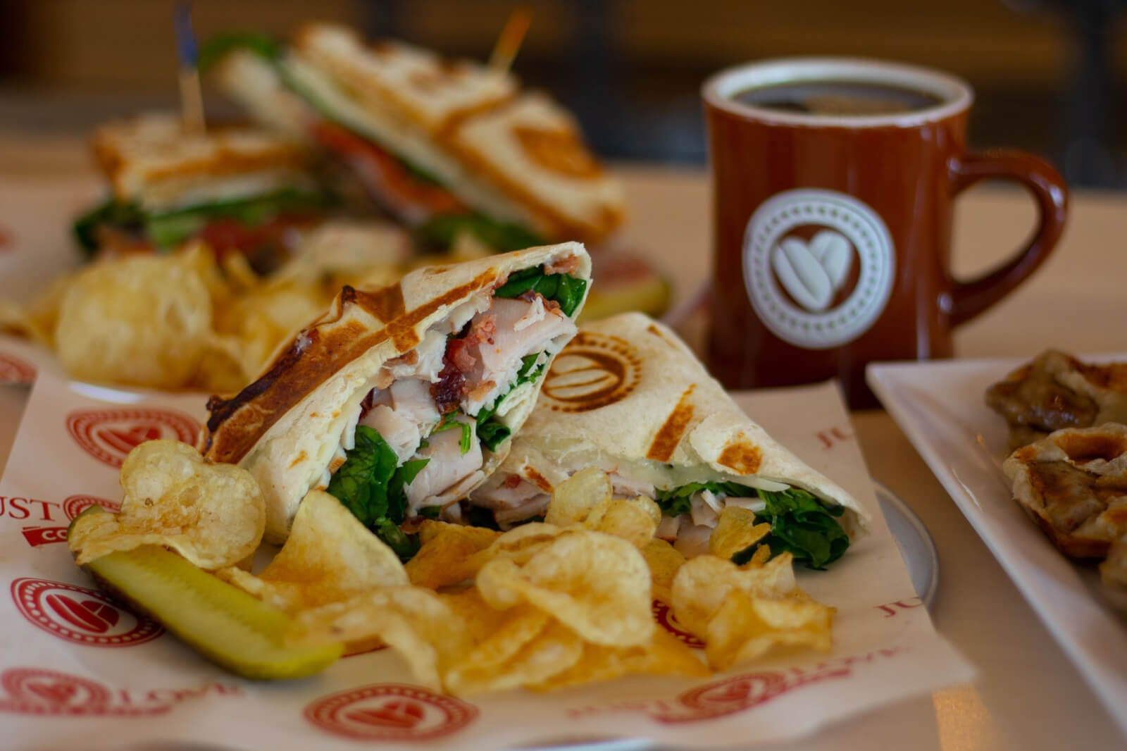Plate of sandwich, pickle, and chips, next to a mug of coffee