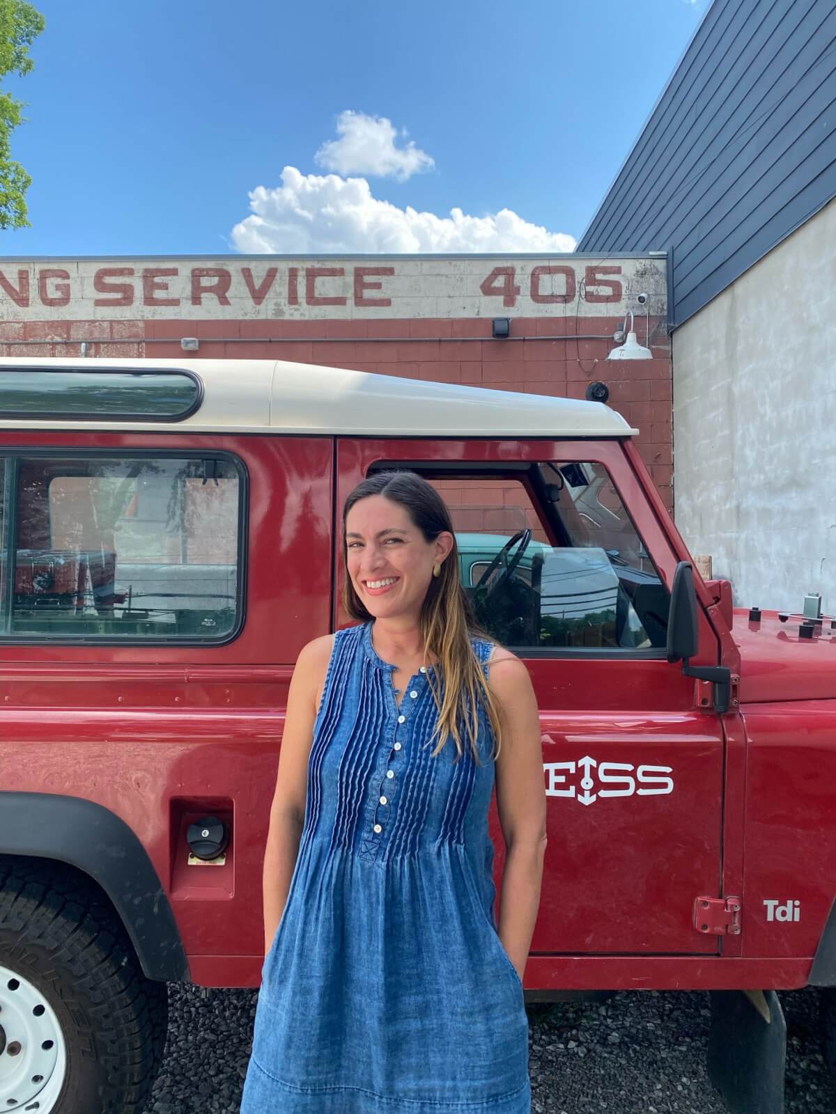 Woman in blue dress, standing in front of red truck that says "Weiss"