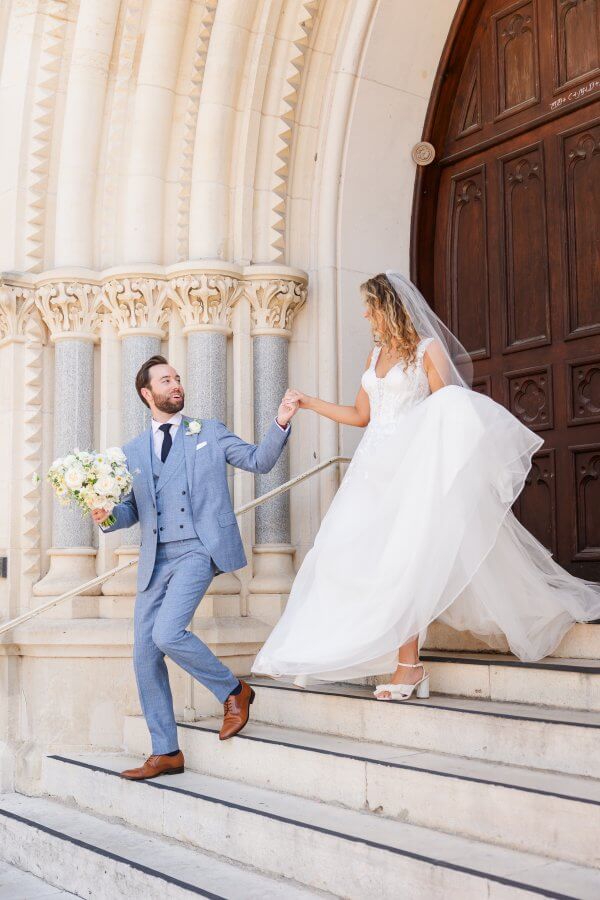 Bride and groom walk down the steps of a stately Catholic shurch