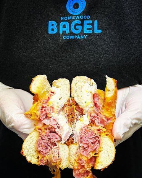Homewood Bagel baker holds a stuffed meat and cheese bagel sandwich.