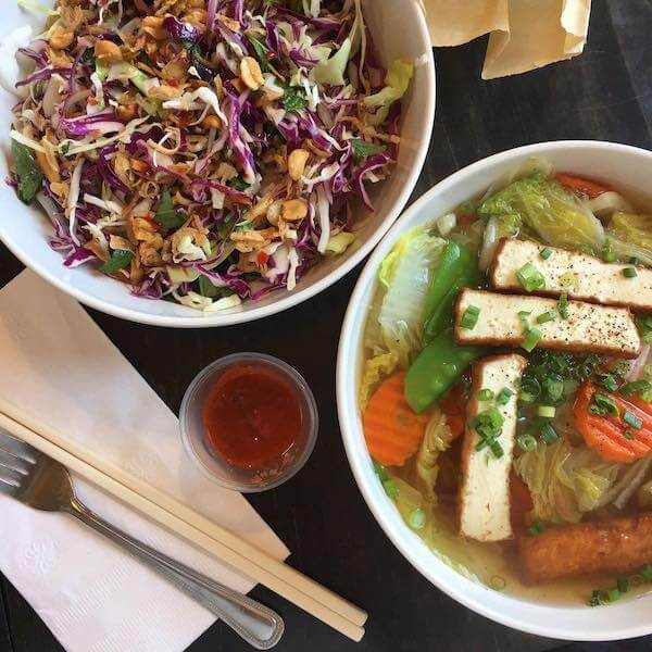 two Vietnamese dishes in round white bowls next to a fork and chopsticks