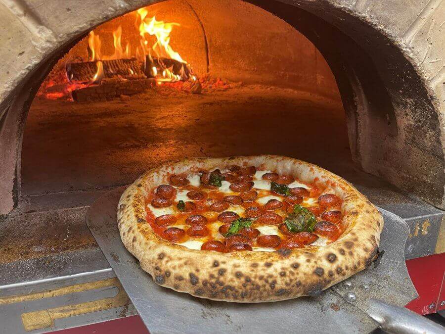 pizza getting pushed into a wood-fired oven