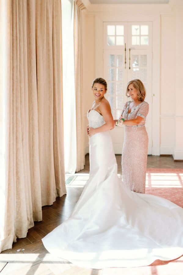 bride and mother of the bride buttoning wedding dress