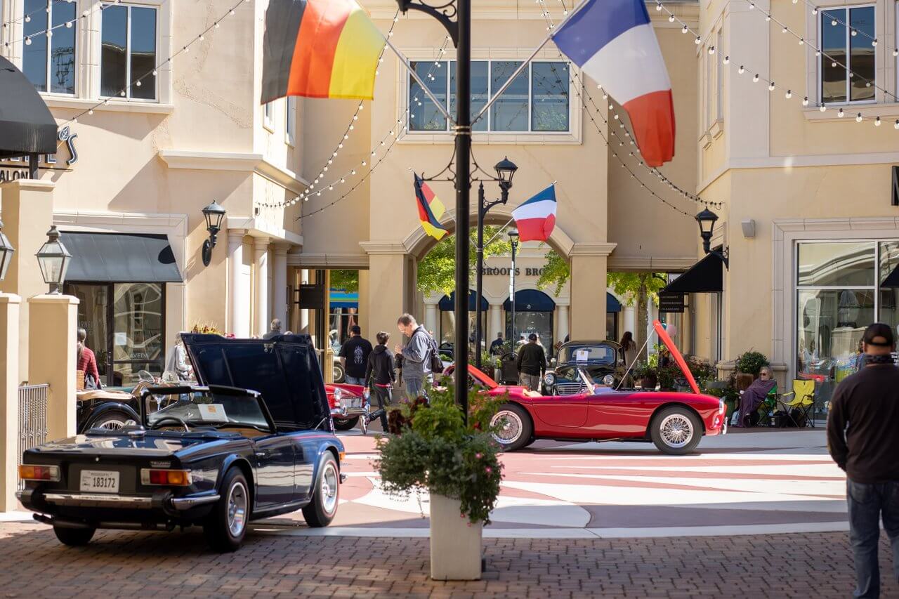 Classic cars on display in plaza at open-air shopping center.