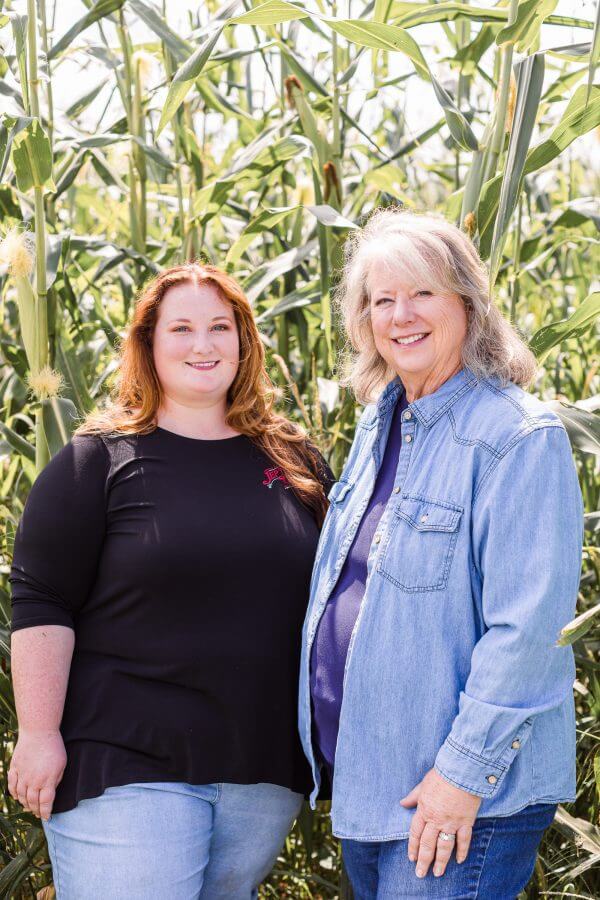 Autumn and Joyce Netherly smile in front of large corn crops