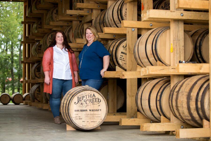 Autumn and Joyce Netherly stand in front of bourbon barrels.