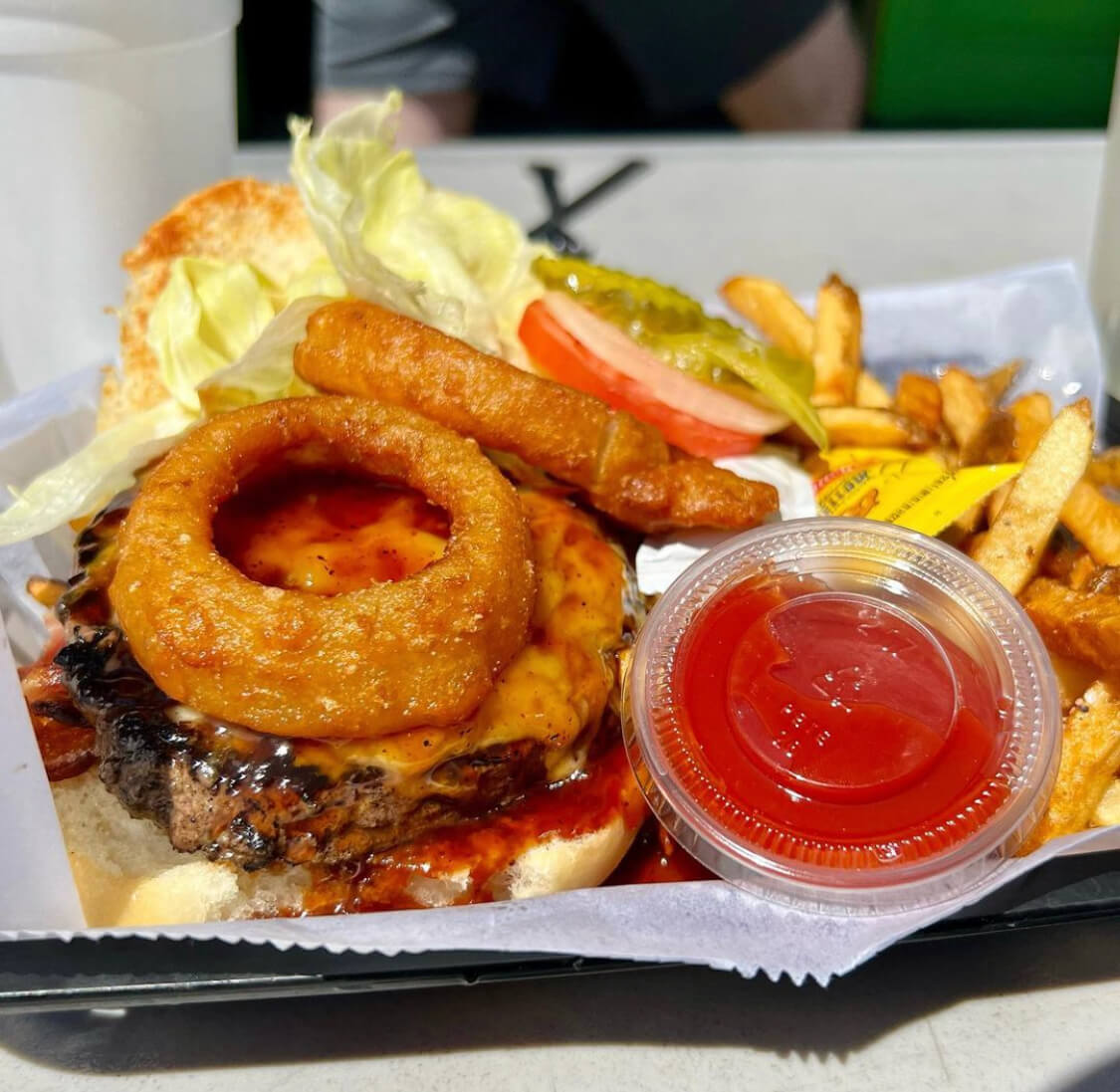 Burger topped with cheese and onion rings, served with fries