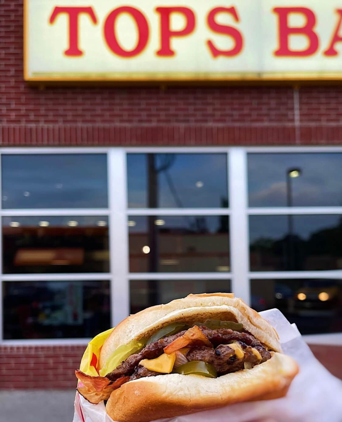 Burger being held in front of restaurant exterior