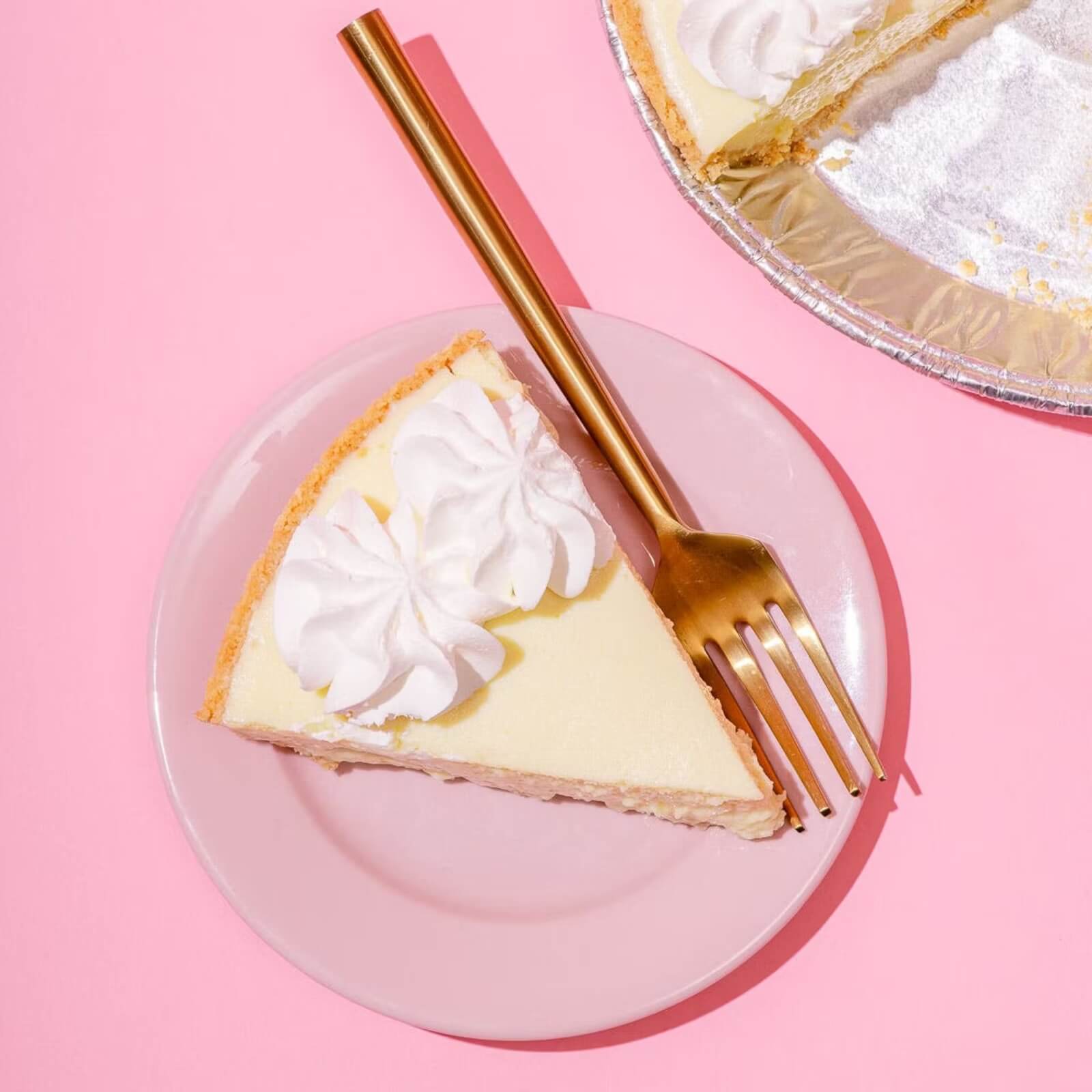 A slice of cream pie with whipped topping sits on a pink plate with a gold fork, next to a partially eaten pie—just like the kind you’d find at southern restaurants that ship their sweet treats nationwide.