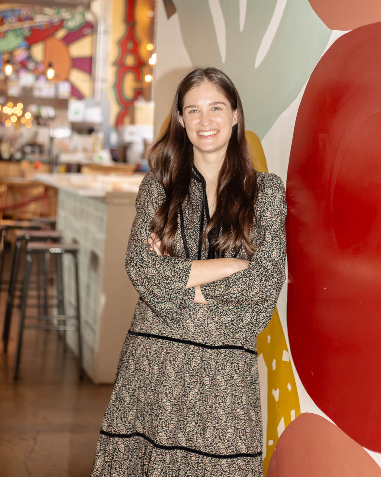 Brunette woman in a dress, smiling against a colorful wall