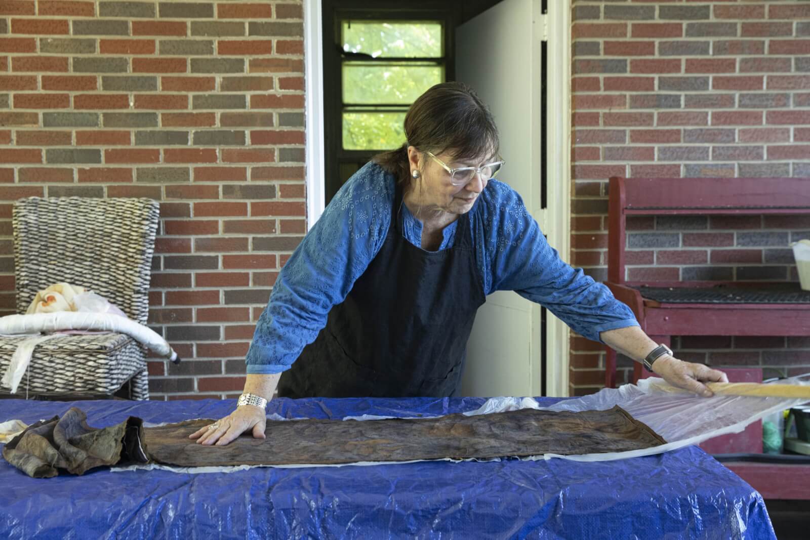 Woman dyeing fabric outside of a brick home.