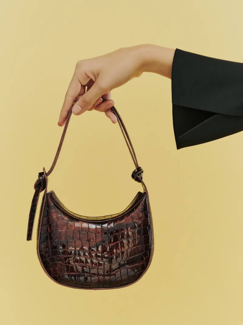 hand holding crocodile shoulder bag in front of yellow background