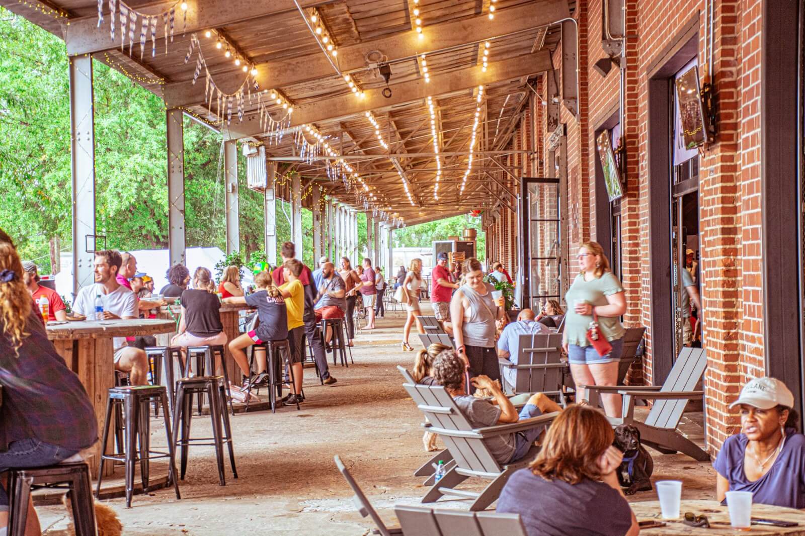 Crowded outdoor patio area with people sitting at tables and in lawn chairs