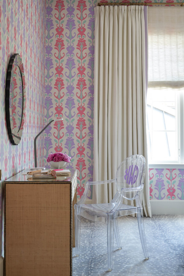 Bedroom desk with lucite chair in front of pink and purple patterned wallpaper