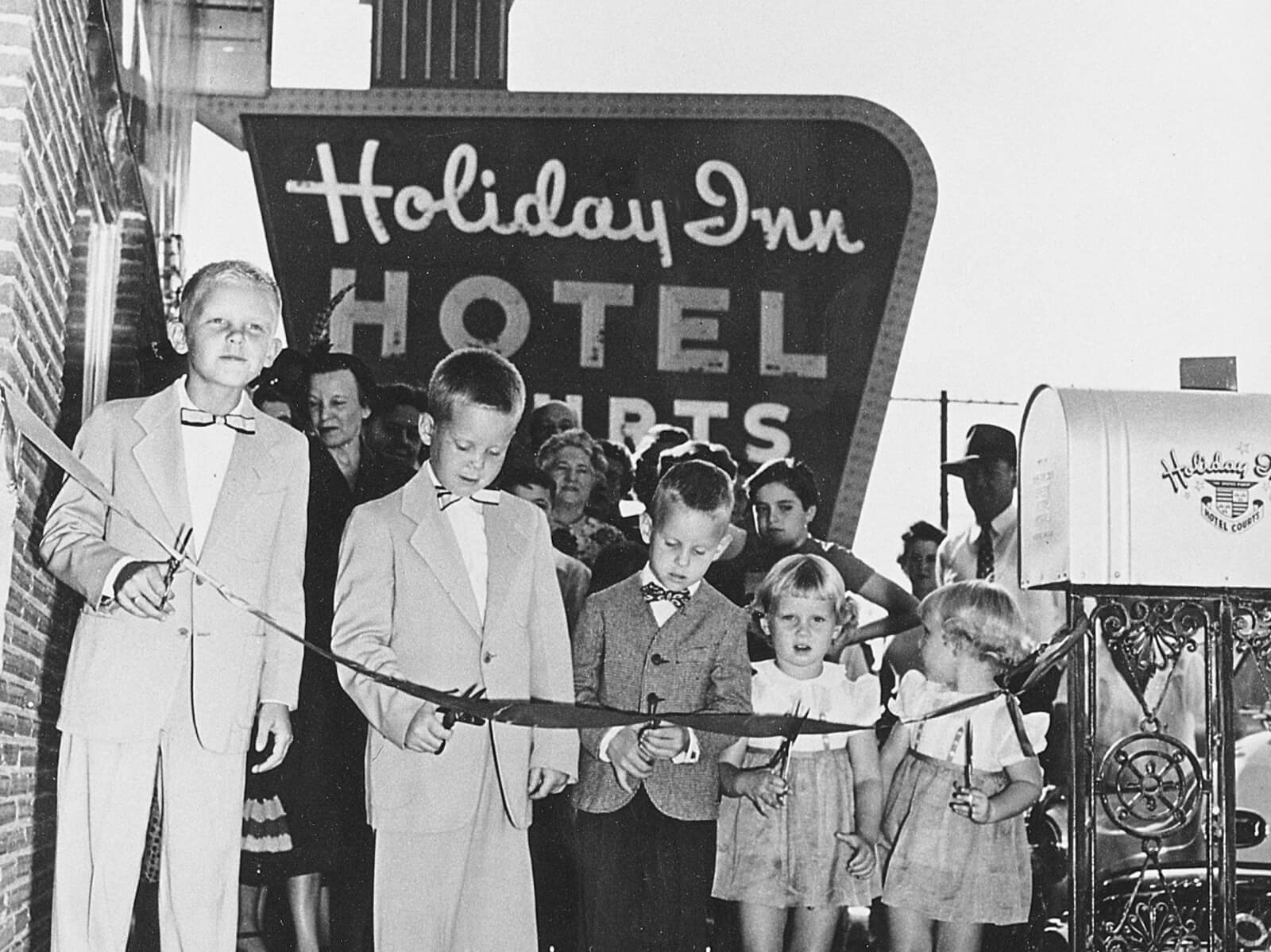 Black and white photo ribbon cutting with children in front of a Holiday Inn