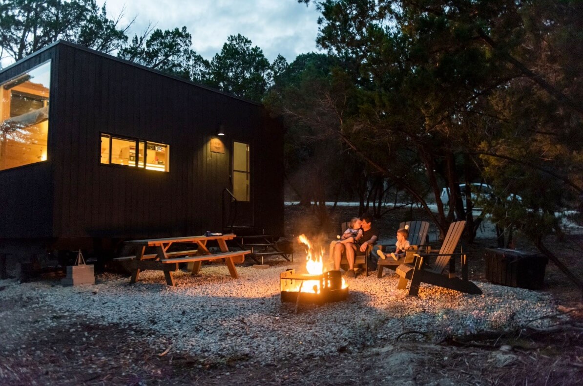 family sitting outside a cabin at night by a fire pit