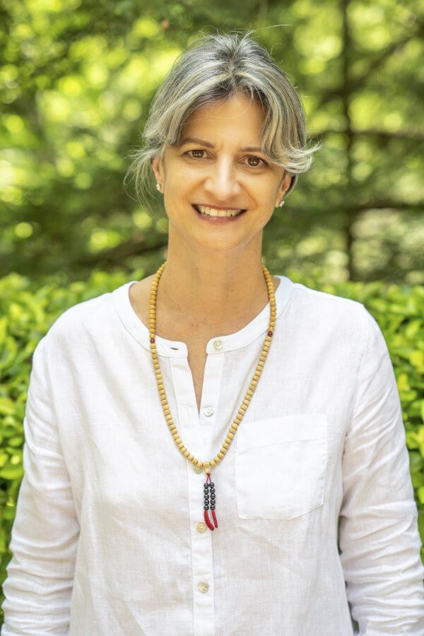 Woman with gray hair in a white blouse, in front of foliage