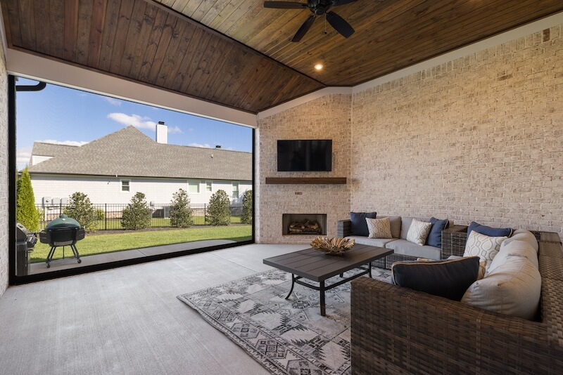 back porch with sofa, table, and TV overlooking grill patio and backyard.