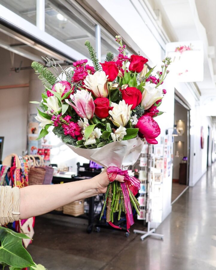 Your Updated Guide to Crosstown - 5 A hand holds a bouquet of red roses, white lilies, and pink flowers wrapped in white paper inside the bright, modern Crosstown Concourse market.