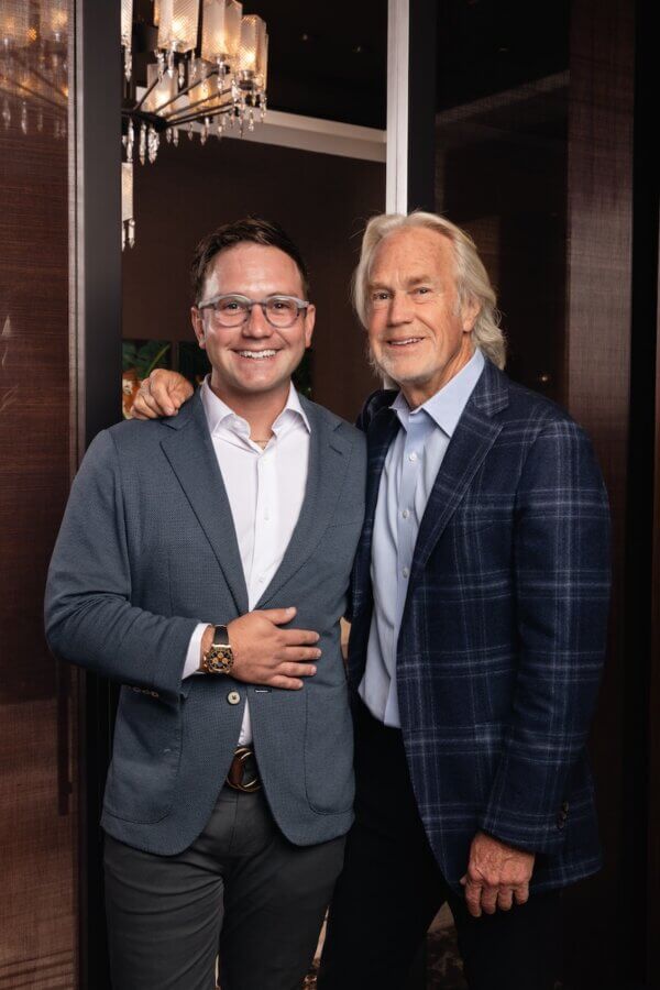 Discover Nashville’s Luxury Secret - 2 Two men in blazers stand side by side indoors at Diamond Cellar, smiling at the camera. One has his arm around the other. A chandelier and dark wood paneling create a warm, elegant backdrop.
