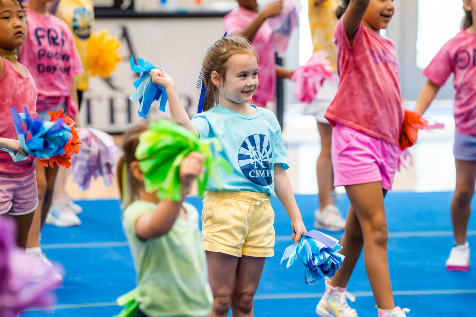 Children are cheerfully participating in a dance class at one of the vibrant Nashville summer camps, holding colorful pom-poms on a blue mat.