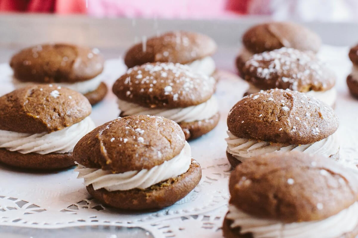 Whoopie pies with chocolate cookies and vanilla cream filling are displayed on a lace doily, sprinkled with powdered sugar, offering a sweet treat reminiscent of the delightful surprises often found in Memphis adult education classes.