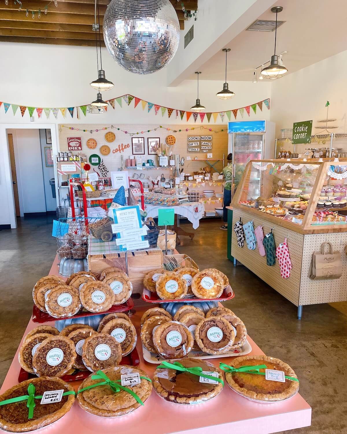 A bakery interior with a variety of pies on a central display table, whimsically decorated with a disco ball overhead.