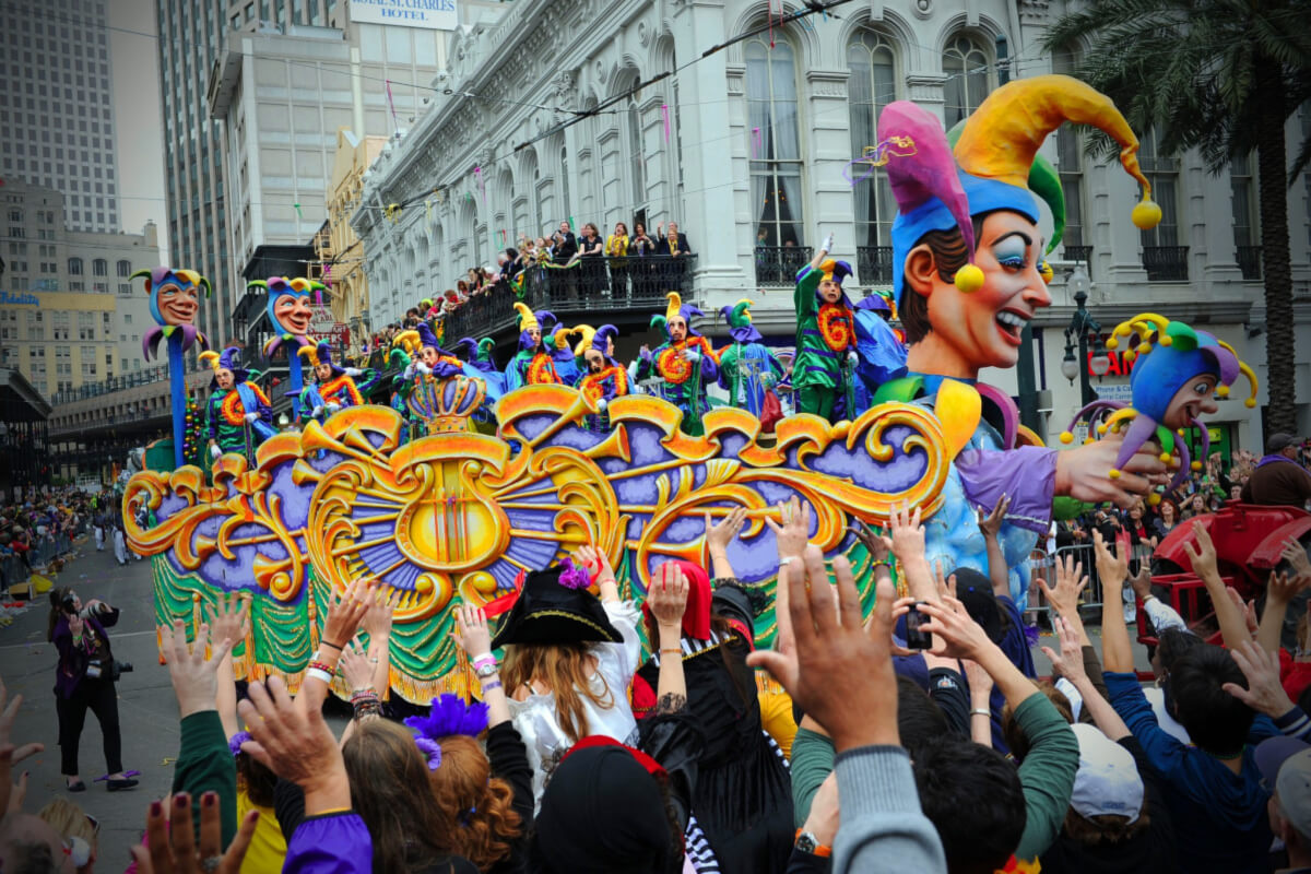 A vibrant Mardi Gras parade float with jester figures glides through the city streets in February during one of the most lively Southern events, as a crowd eagerly stretches to catch throws.