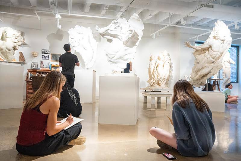 In an art gallery, people keenly observe and sketch large white sculptures displayed around the room, evoking the creativity often fostered in Nashville summer camps.