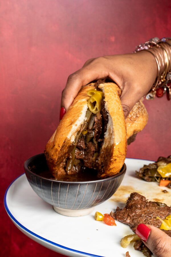 Woman holding a vegan Italian sandwich and dipping it in sauce