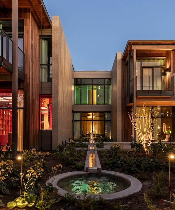 23 New Boutique Hotels in the South - 12 This modern building exterior blends glass windows with wooden elements. It features a central pathway, a small round pond, and a landscaped garden, all beautifully illuminated by evening lights.