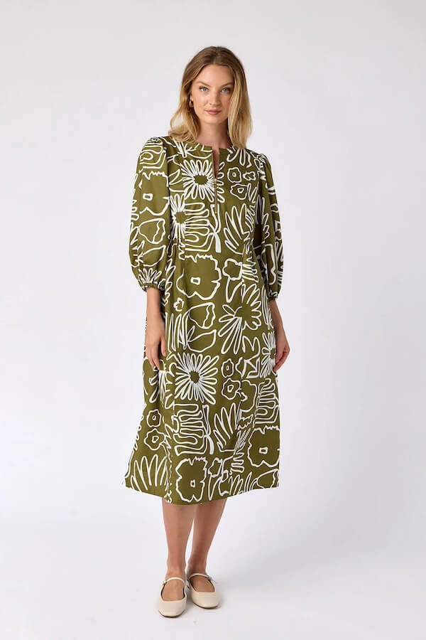 Woman in a green dress with white floral patterns, standing against a plain background, reminiscent of a Southern belle's charm in early February.